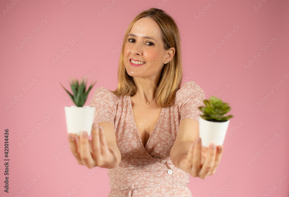 Young beautiful woman holding two small plants pot over isolated pink background Young beautiful woman holding two small plants pot over isolated pink background
