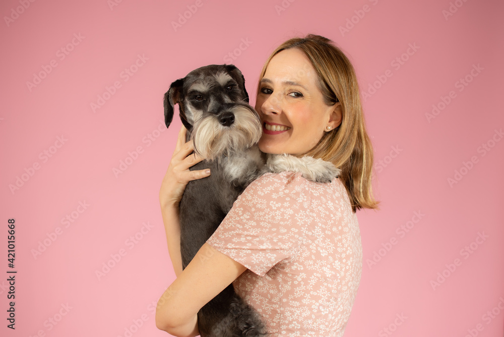 Cute young woman hugs her puppy schnauzer dog. Love between owner and dog isolated over pink background. Studio portrait. Cute young woman hugs her puppy schnauzer dog. Love between owner and dog isolated over pink background. Studio portrait.