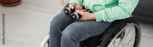 Cropped view of handicapped woman in wheelchair holding dumbbells at home, banner