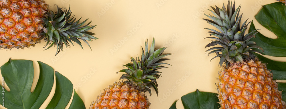 Fototapeta premium Top view of fresh pineapple with tropical leaves on yellow background.