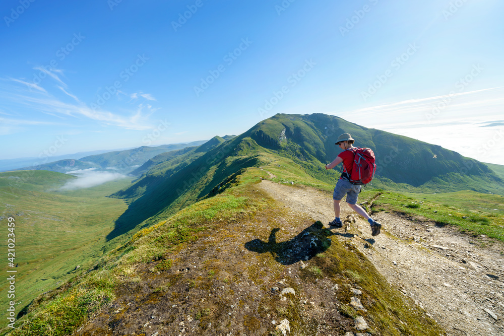 A female hiker walking, hiking along a mountain path towards the summit of Ben Lawers from the top of Beinn Ghlas in the Scottish Highlands, UK landscape.