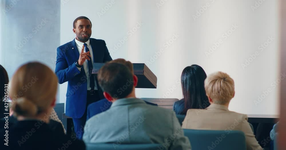 Young successful African American businessman speaking in front of audience at session and answers questions. Press conference concept. Young successful African American businessman speaking in front of audience at session and answers questions. Press conference concept.