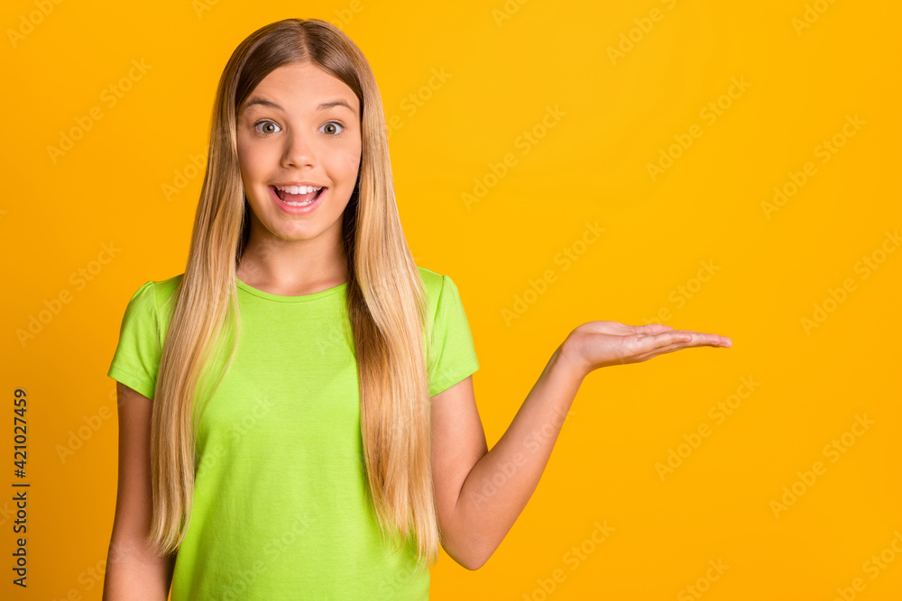 Photo of young excited girl happy smile show present product offer advert promo isolated over yellow color background Photo of young excited girl happy smile show present product offer advert promo isolated over yellow color background