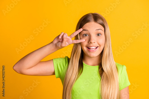 Photo of young school girl happy positive smile show peace cool v-sign isolated over yellow color background