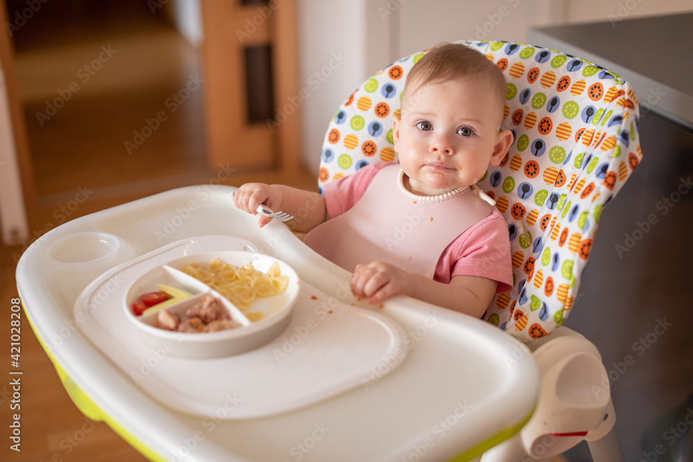 One year old girl having balanced meal in baby eating chair, healthy balanced nutrition for child One year old girl having balanced meal in baby eating chair, healthy balanced nutrition for child