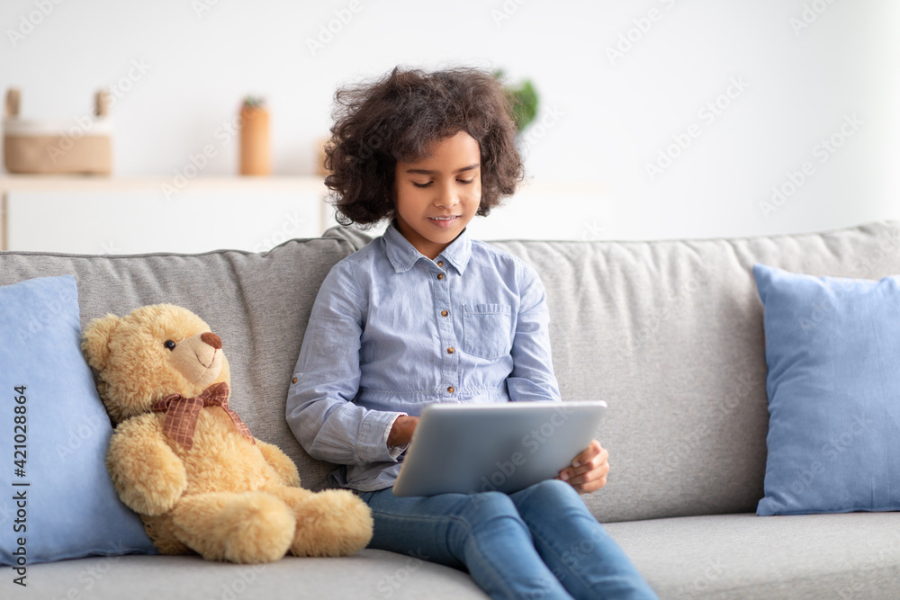 Afro girl using digital tablet, sitting on sofa Afro girl using digital tablet, sitting on sofa