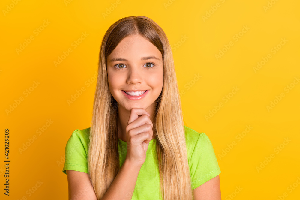 Photo of young attractive school girl happy positive smile think hand touch chin isolated over yellow color background Photo of young attractive school girl happy positive smile think hand touch chin isolated over yellow color background
