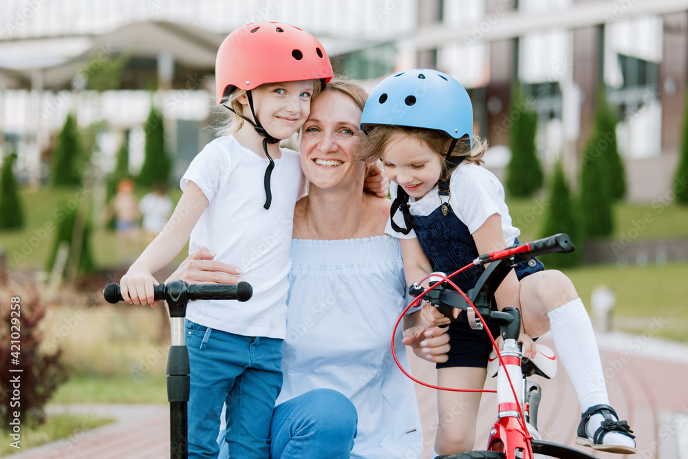 Naklejka premium Mother with two chherful daughters having fun. Woman and girls in helmets riding on bicycle and scooter