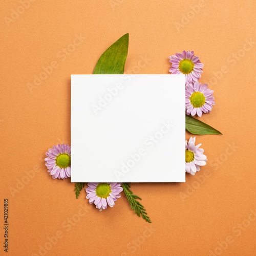 White memo pad with pink flowers on orange background. flat lay  top view  copy space