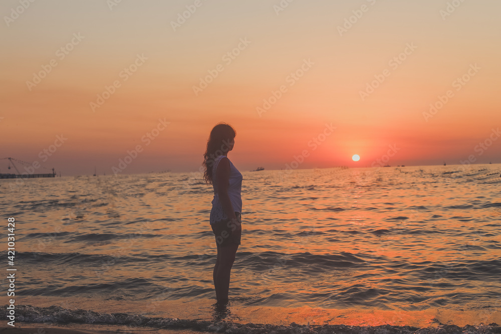 concept of tourism presented by a girl standing in front of orange sunset