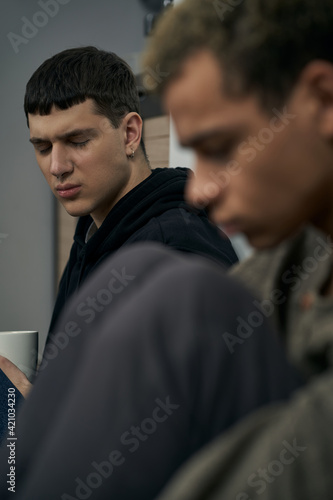 Staged photo illustrates problems and conflicts in gay couple relationships. Moment of showdown: two young men are sitting on the floor near each other. Partners are upset and wistful.