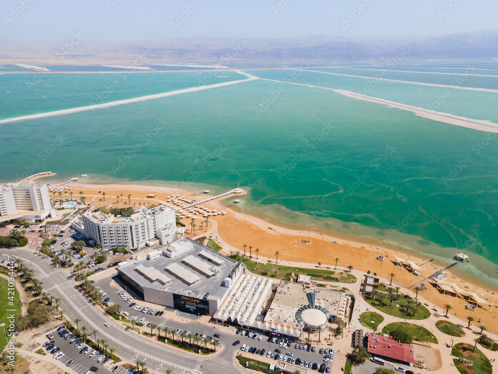 Aerial view from a drone of the beach on the Ein Bokek embankment on the coast of the Dead Sea, the sea itself and the mountains of Jordan visible in the distance, in Israel