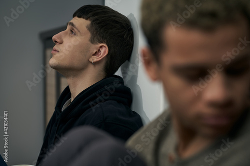 Staged photo illustrates problems and conflicts in gay couple relationships. Moment of showdown: two young men are sitting on the floor near each other. Partners are upset and wistful.