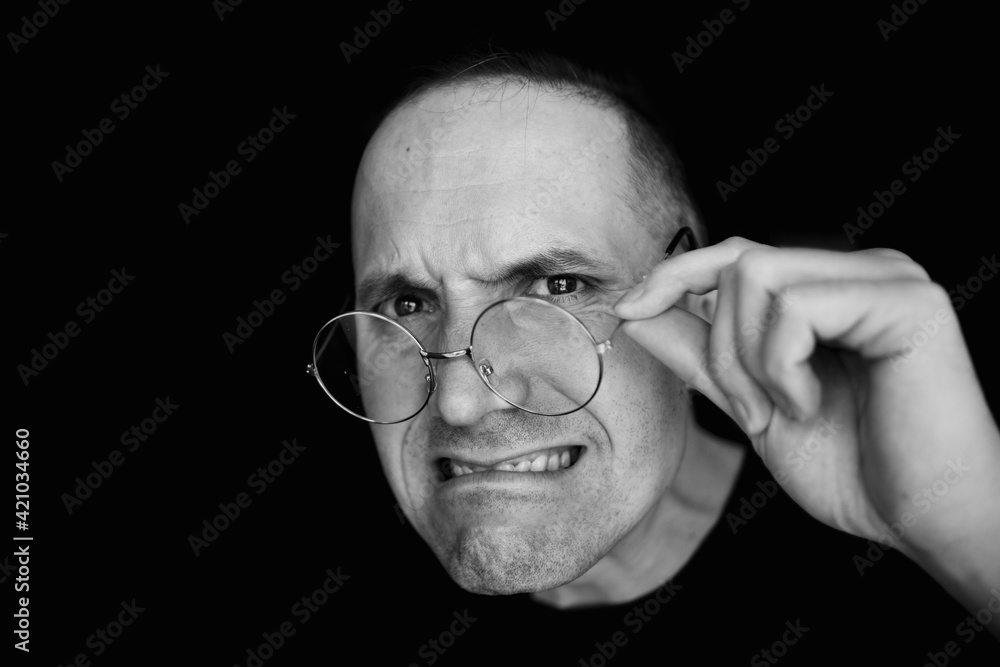 Fototapeta premium Black and white photo of a portrait of a young man with glasses. Holds her bangs with her hand. Close your forehead. On a black background. He holds his glasses. A serious face. Businessman.