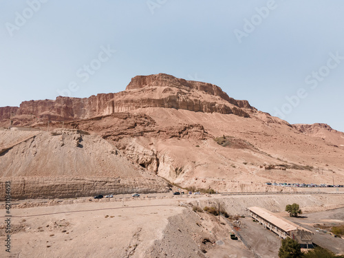 A sandy mountain that used to be bottom of Dead Sea stands near Ein Bokek embankment on the coast of the Dead Sea, the sea itself and the mountains of Jordan visible in the distance, in Israel