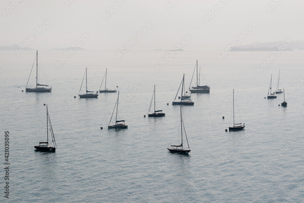 Silhouettes of anchored sailing boats in the mist