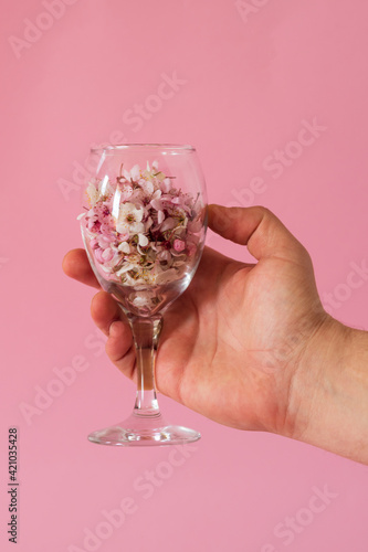 A man's hand holding a wine glass filled with flowers. Spring concept.
