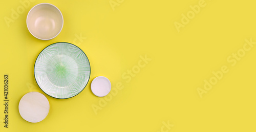 Mock up table setting on yellow background. Group of ceramic utensile with plate, bowl and sauser for summer serving or restaurant menu. Minimalist style. Trendy color. Banner