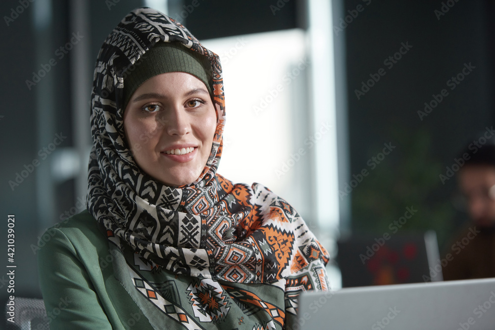 Portrait of beautiful muslim woman in hijab smiling at camera while sitting at office Portrait of beautiful muslim woman in hijab smiling at camera while sitting at office