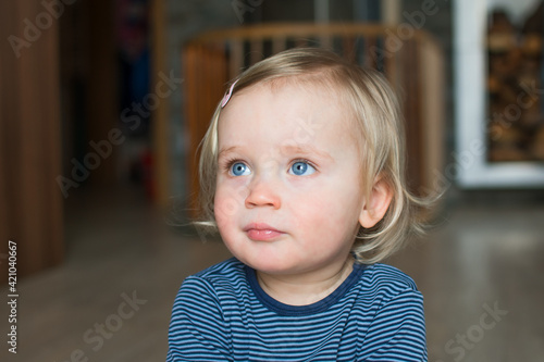 Cute caucasian baby face with blond hair and blue eyes, close up portrait. Small kid posing at home. Indoor portrait with copy space.