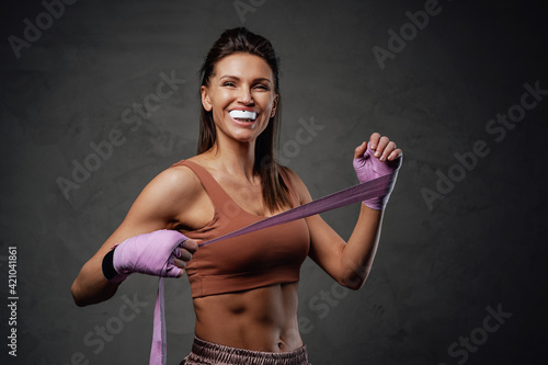 Fotografia Smiling sportswoman poses in dark background with bandages