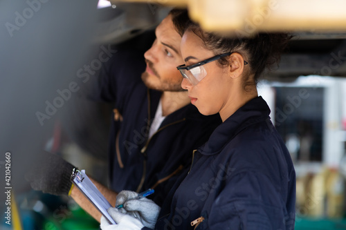 Hispanic Female trainee Mechanics Working Underneath Car Together Car maintenance and auto service garage. Car maintenance and auto service garage concept. photo