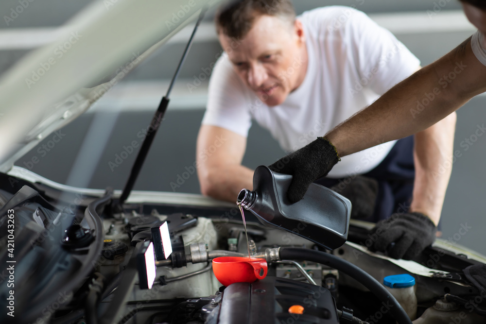 Pouring oil to car engine. Closue up male mechanic hand working and service in Car Service station Pouring oil to car engine. Closue up male mechanic hand working and service in Car Service station