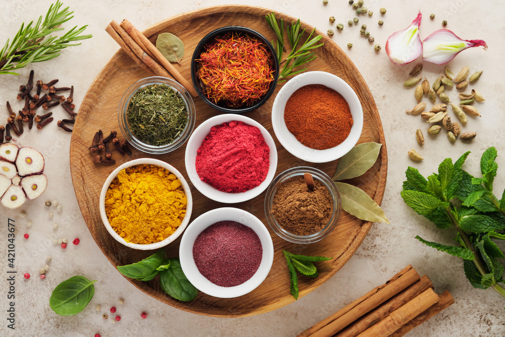 Colorful herbs and spices for cooking: turmeric, dill, paprika, cinnamon, saffron, basil and rosemary. Indian spices in wooden plate. On light brown stone background. Top view.