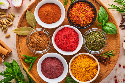 Colorful herbs and spices for cooking  turmeric  dill  paprika  cinnamon  saffron  basil and rosemary. Indian spices in wooden plate. On light brown stone background. Top view.