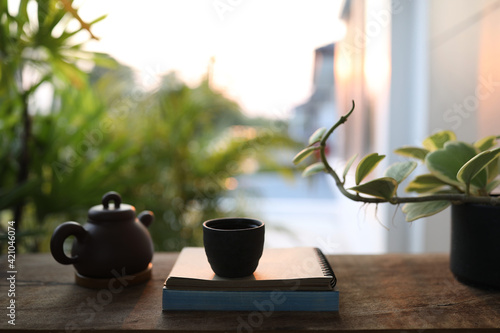 Black tea cup and teapot with notebook and plant on wooden table