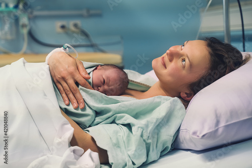 Mother and newborn. Child birth in maternity hospital. Young mom hugging her newborn baby after delivery. Woman giving birth.