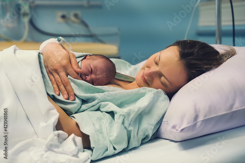 Mother and newborn. Child birth in maternity hospital. Young mom hugging her newborn baby after delivery. Woman giving birth. photo