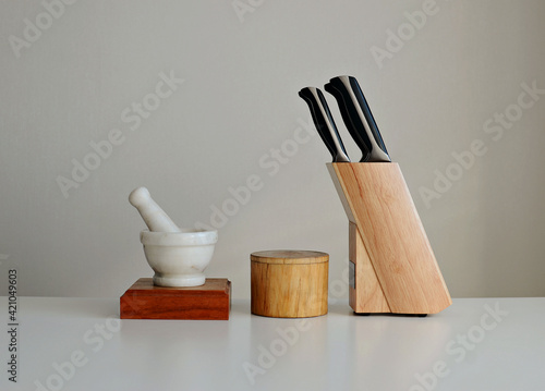 Set of knives on a wooden stand, mortar and pestle, wooden bowl on a white background. Interior mockup, copy space.