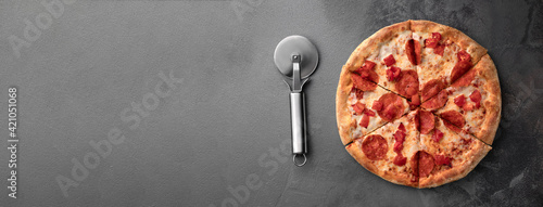 whole fresh round pizza with pepperoni and mozzarella cheese and knife on a gray table top view. tasty fast food banner background in pizzeria, copy space
