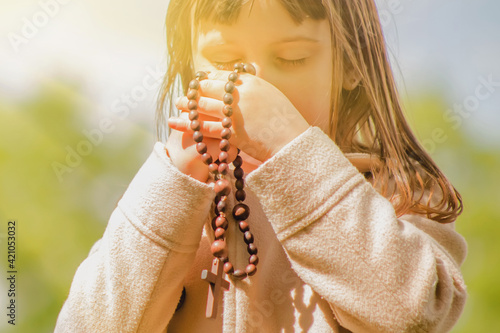 Papier peint Little child girl praying with wooden rosary. Selective focus.