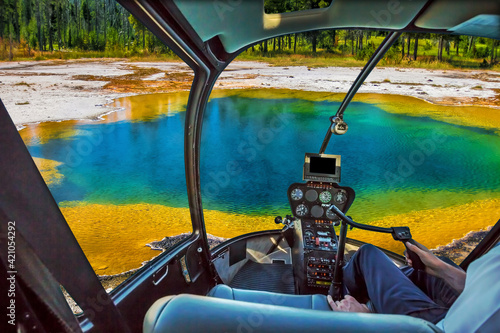 Helicopter cockpit with pilot arm and control console inside the cabin flight over colorful Abyss Pool in the West Thumb Geyser Basin of Yellowstone National Park, Wyoming, United States.
