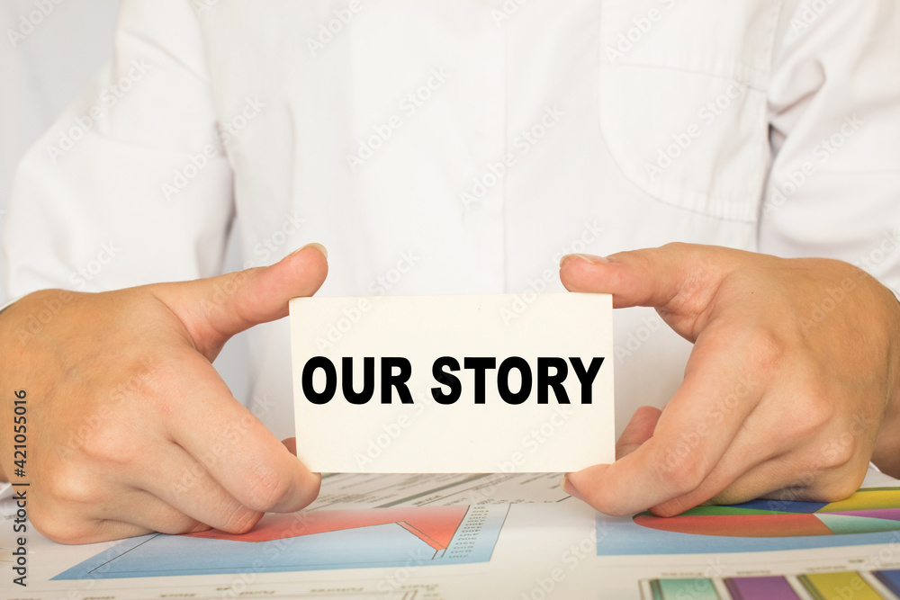 a man in the office holds a card with text OUR STORY . business concept a man in the office holds a card with text OUR STORY . business concept
