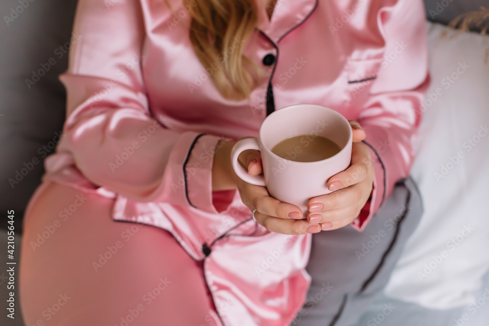 Young woman holding a pink mug with coffee in her hands Pink pajamas in the apartment Painted nails Young woman holding a pink mug with coffee in her hands Pink pajamas in the apartment Painted nails