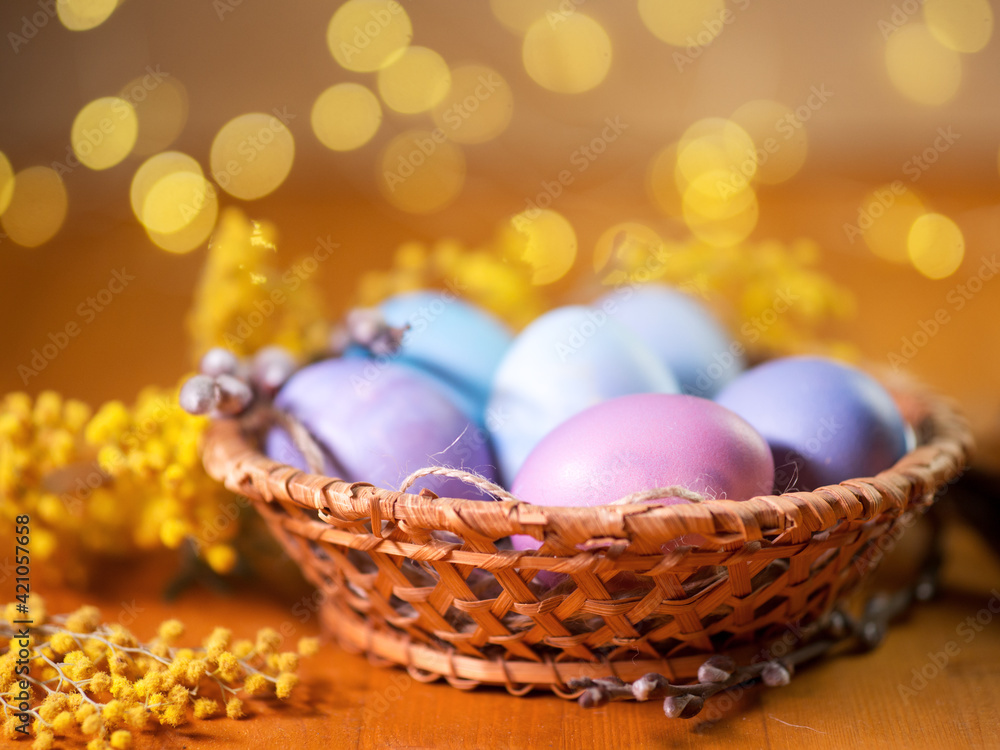 Close-up of Easter eggs in a wicker basket on a wooden table. Colorful pastel egg colors