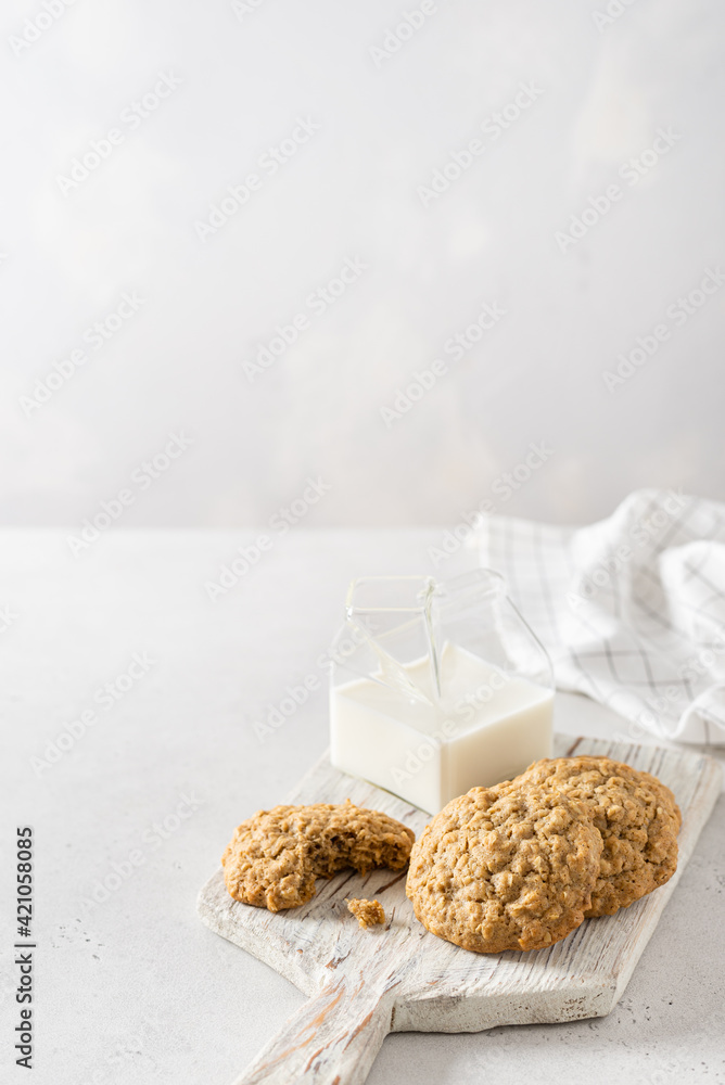 A stack of homemade cookies with cereals and seeds. Oatmeal crackers or biscuits on a wooden board and a cup of milk on white background. Copy space. Recipe, menu