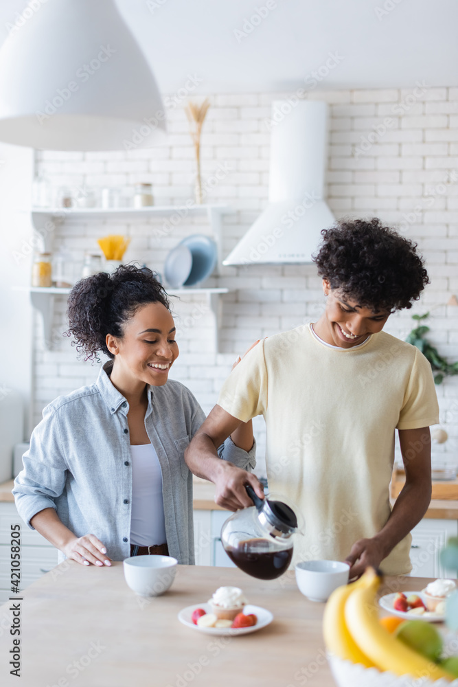 Smiling african american woman standing near boyfriend pouring coffee and tasty breakfast Smiling african american woman standing near boyfriend pouring coffee and tasty breakfast