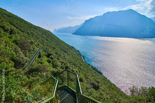 Panoramic view on Lake Garda from the Busatte-Tempesta trail near Nago-Torbole with the iron staircase,  Torbole  town surrounded by mountains in the summer time,Italy