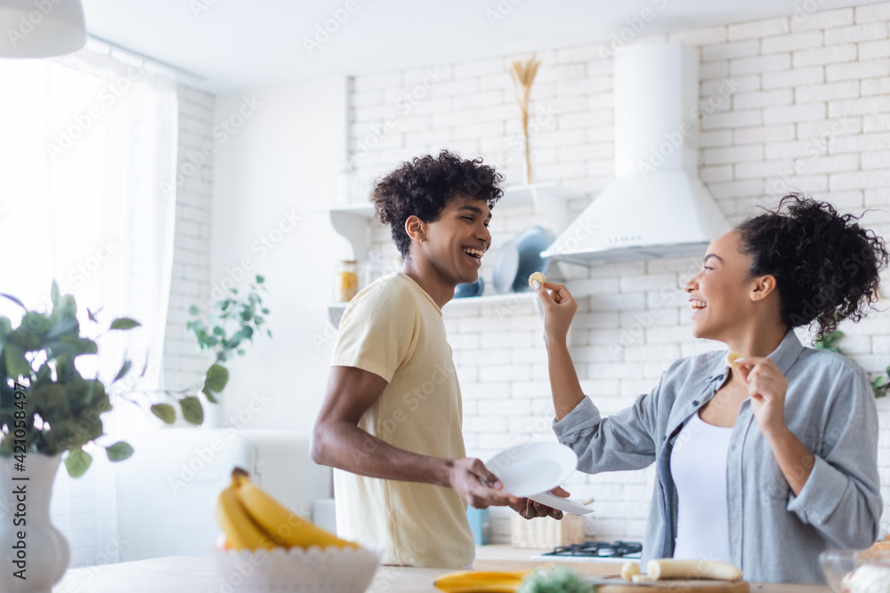 Cheerful african american couple with plates and banana in kitchen