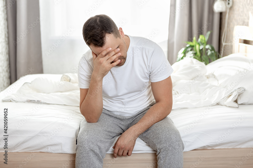 Frustrated man sits on a bed in his bedroom Frustrated man sits on a bed in his bedroom