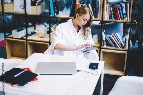 Serious woman browsing tablet in library