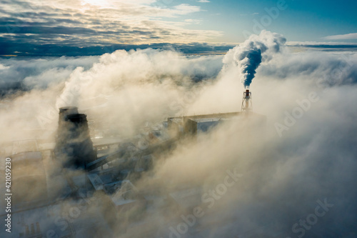 large clouds of white smoke cover power plant territory under bright sunlight on frosty winter day aerial view