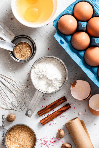 Baking ingredients and kitchen utensils on a white background top view. Baking background. Flour, eggs, sugar, spices, and a whisk on the kitchen table. Flat lay.