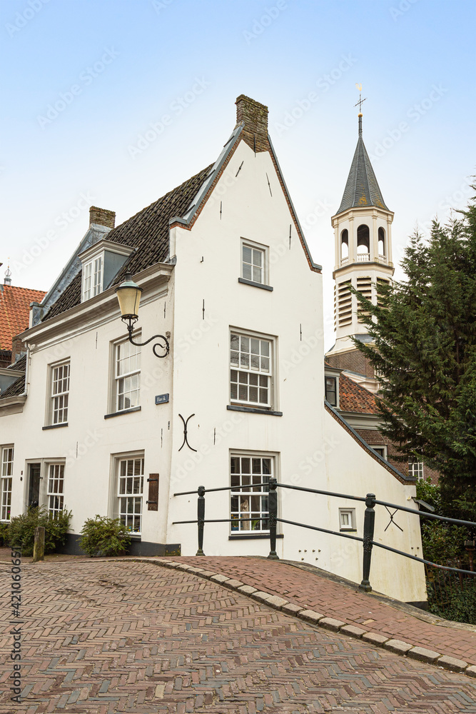A picturesque white house near the bridge over the canal with a church tower in Amersfoort in the background.