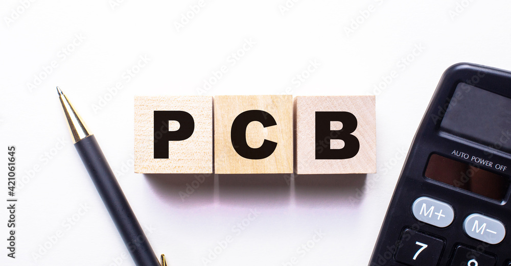 The words PCB is written on wooden cubes between a pen and a calculator on a light background. The words PCB is written on wooden cubes between a pen and a calculator on a light background.
