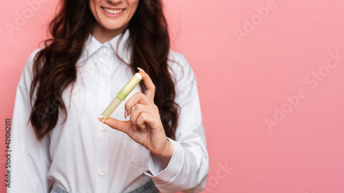 A young woman holds a menstrual swab with an applicator in her hands for easy use. Pink background. Space for text. The concept of feminine hygiene.